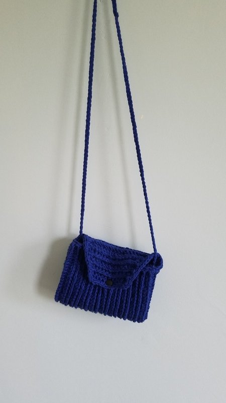 Blue crocheted shoulder bag with braided strap hanging on a wall