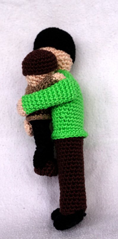 Zwei gehäkelte Amigurumi-Figuren umarmen sich, eine mit grünem Oberteil und braunen Hosen