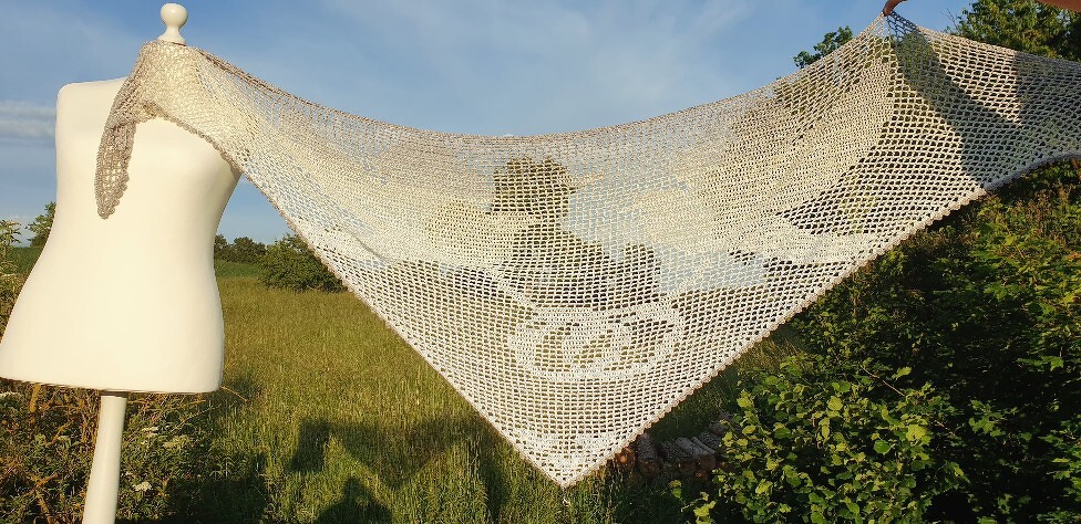 Dreieckiges helles Filet-Häkeltuch mit Hochzeitsmotiv auf Schaufensterpuppe im Freien