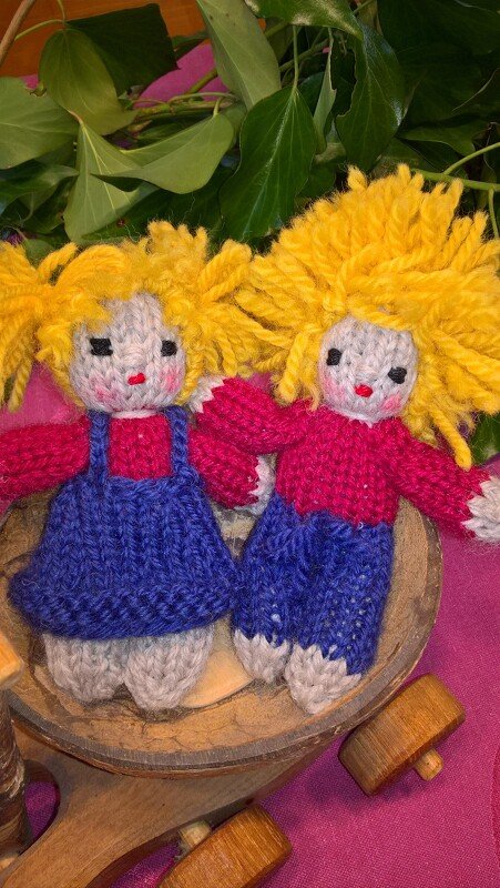 Zwei gestrickte Amigurumi-Puppen mit gelbem Haar in einer Holzschale