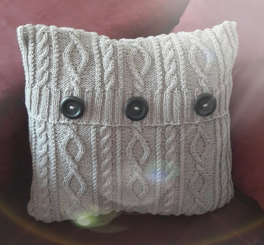 Heller gestrickter Kissenbezug mit Zopfmuster und drei dunklen Knöpfen