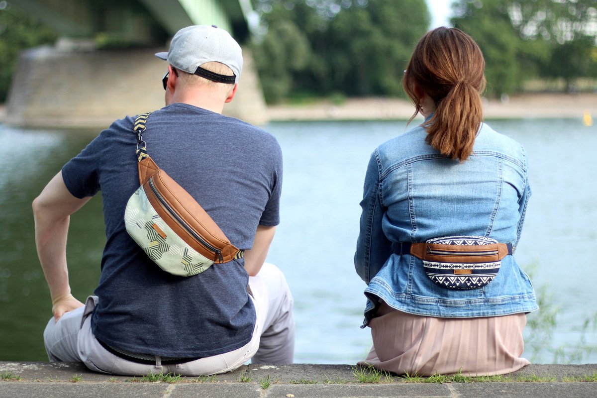 Zwei Personen von hinten mit gemusterten Bauchtaschen: eine hellgrün mit geometrischem Muster, die andere dunkelblau mit Tribal-Muster.