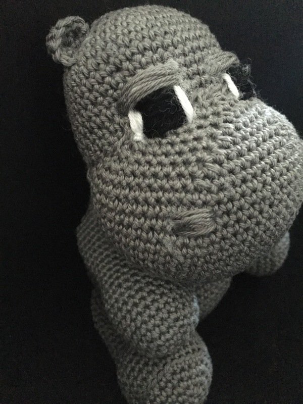 Gray crocheted hippo amigurumi with white teeth on black background