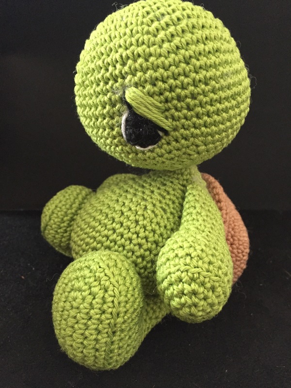 Small green crocheted amigurumi turtle with brown shell, one eyelid lowered