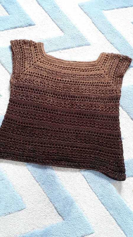 Ärmelloses gehäkeltes Damen-Shirt in Braun mit Ombré-Effekt und Lochmuster auf hellblau-weiß gemustertem Untergrund liegend.