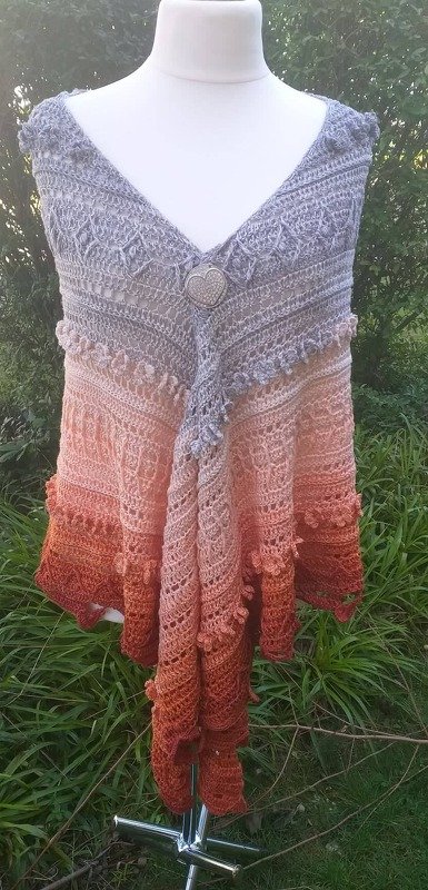 Triangle crochet shawl with grey-to-peach-to-rust gradient and decorative center closure on mannequin