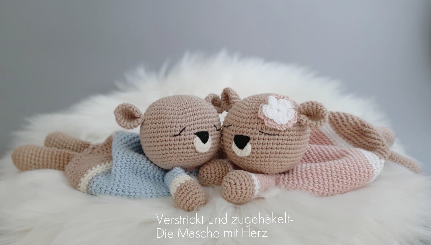 Zwei gehäkelte Babyschmusetücher in Hellblau und Zartrosa auf weißem Flausch