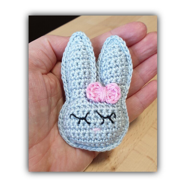 Kleine gehäkelte Häschenfigur in einer Hand, hellblau mit rosa Schleife
