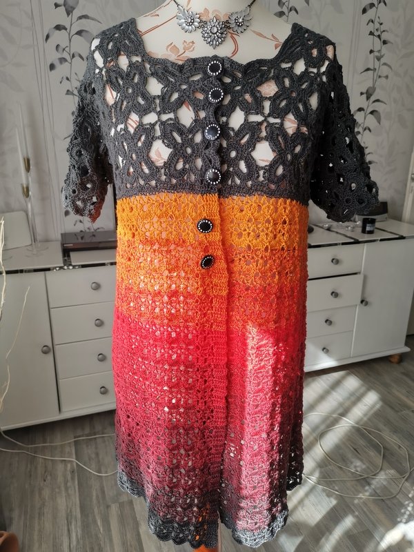 Gehäkelte Kurzarmjacke in Anthrazit, Orange und Rot auf Schneiderpuppe mit sichtbarer Knopfleiste