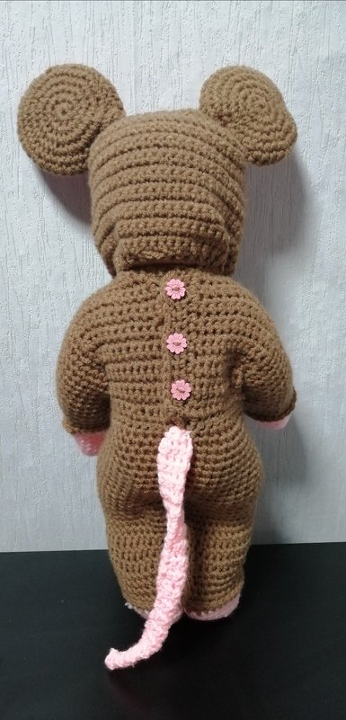 Rückansicht eines braunen, gehäkelten Maus-Kostüms mit Kapuze, runden Ohren, rosa Schwanz und rosa Blumenknöpfen.
