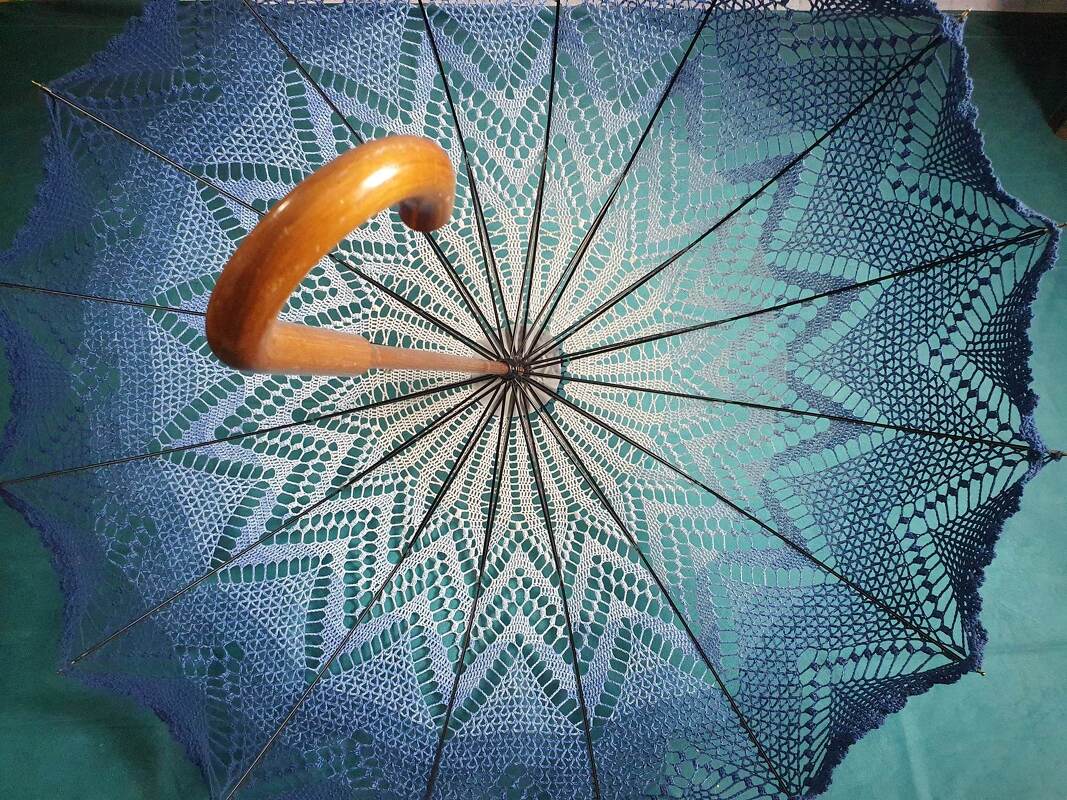 Gehäkelter Sonnenschirm in Blau mit Ombré-Farbverlauf und gebogenem Holzgriff, von oben gesehen.