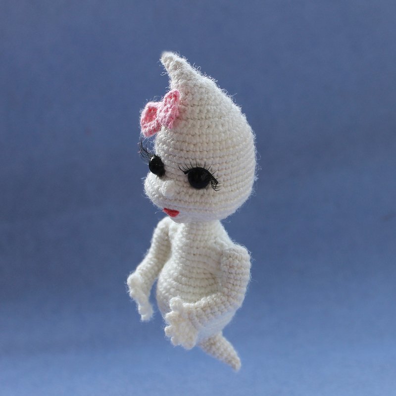 White crocheted amigurumi ghost with black eyes, long eyelashes and pink bow on blue background