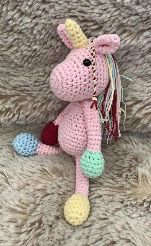 Rosa gehäkeltes Amigurumi-Einhorn mit gelbem Horn und mehrfarbiger Mähne