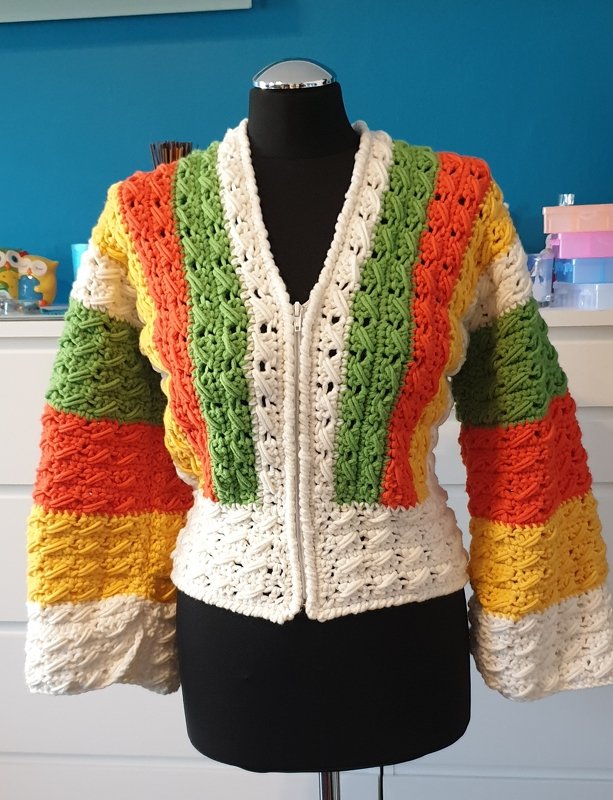 Bunt gestreifte Häkeljacke in Grün, Orange, Gelb und Weiß mit Reißverschluss auf einer schwarzen Schneiderpuppe.