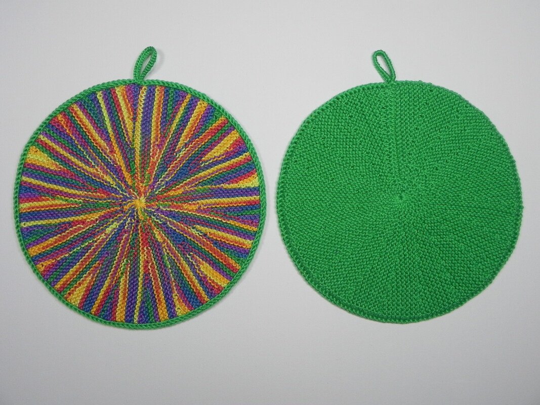 Zwei runde gestrickte Topflappen nebeneinander, links bunt radial gestreift, rechts uni grün, beide mit Aufhängeschlaufe