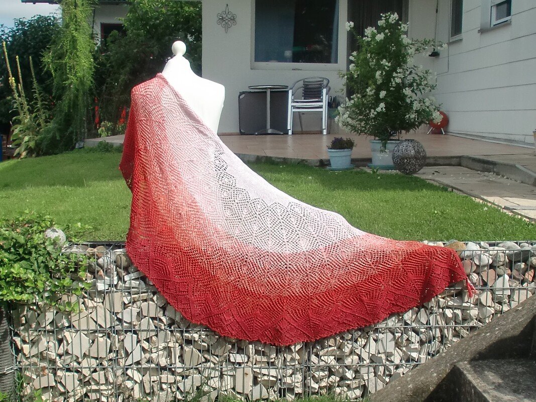 Crescent-shaped lace shawl in red-to-cream gradient draped over a white mannequin outdoors