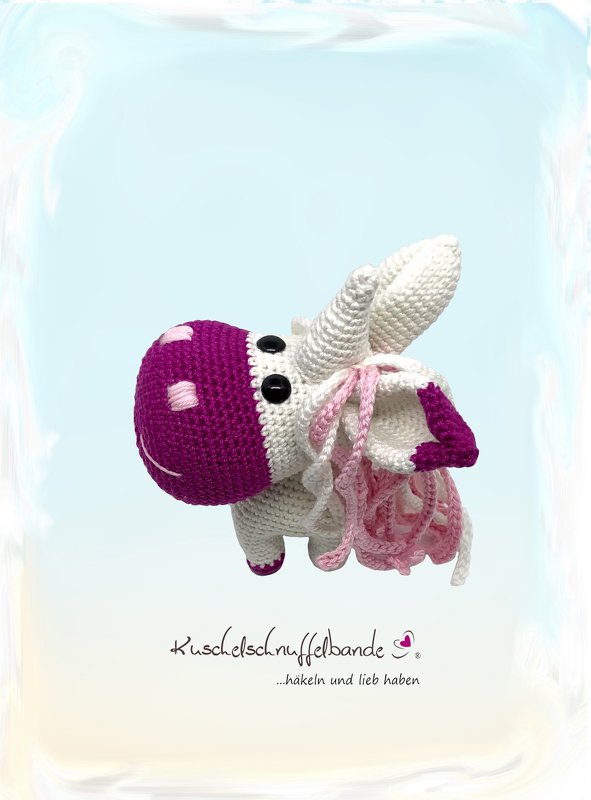 Gehäkeltes Einhorn-Amigurumi mit lila Kopf, rosa-weißer Mähne und schwarzen Augen vor hellem Hintergrund