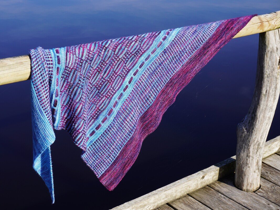 Close-up of a textured knitted triangle shawl with an eyelet band and contrasting stripes