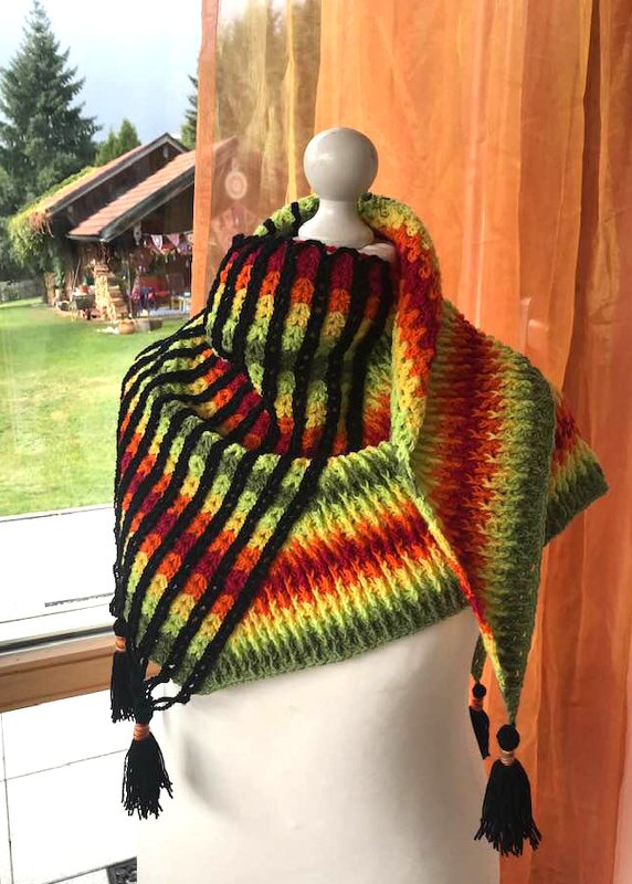 Buntes gehäkeltes Dreieckstuch mit Streifen in Schwarz, Grün, Gelb, Orange und Rot und schwarzen Quasten auf einer Schaufensterpuppe