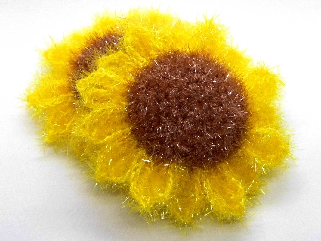Yellow eyelash yarn crochet sunflower scrubby with brown center on white background