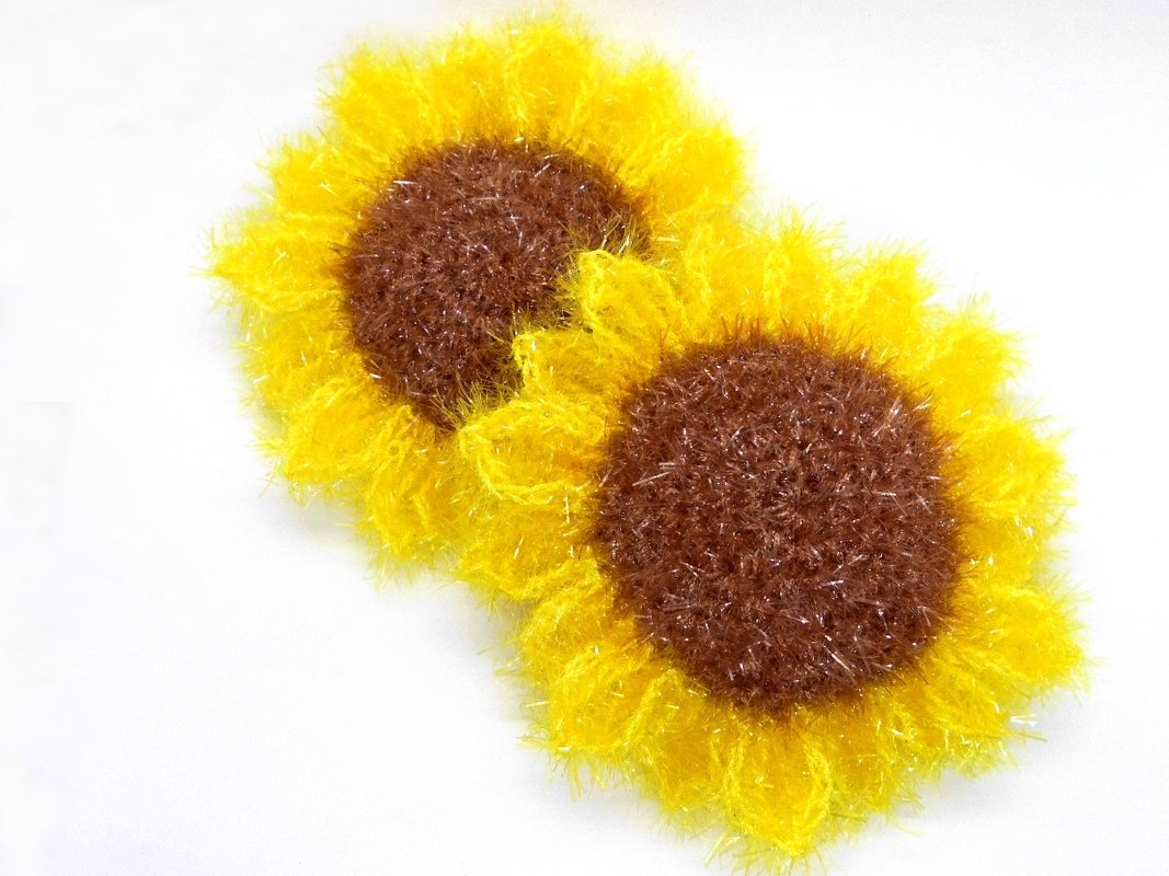 Two crocheted sunflower scrubbies with yellow petals and brown fuzzy centers on a white background