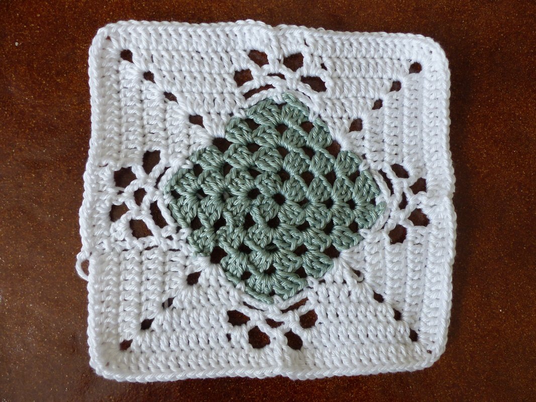 Gehäkeltes Granny Square mit grünem Zentrum und weißem Rand auf braunem Untergrund