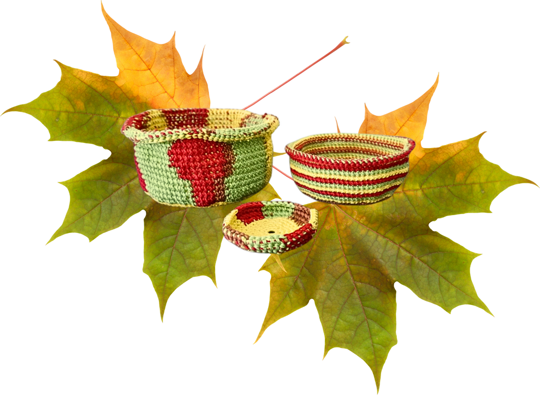 Drei gehäkelte Körbe in Rot, Grün und Gelb auf Ahornblättern
