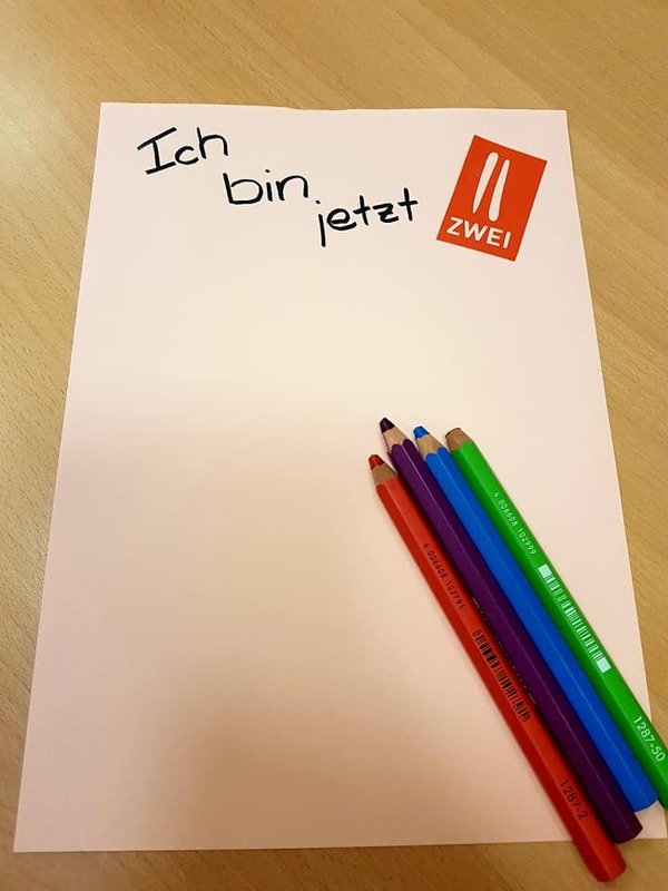 Rosa Papier mit dem Schriftzug 'Ich bin jetzt Zwei' und bunten Buntstiften.
