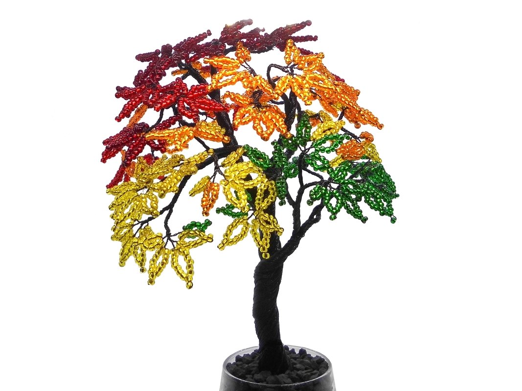 Small beaded wire tree with seed-bead leaves in red, orange, yellow and green, placed in a pot with dark pebbles.