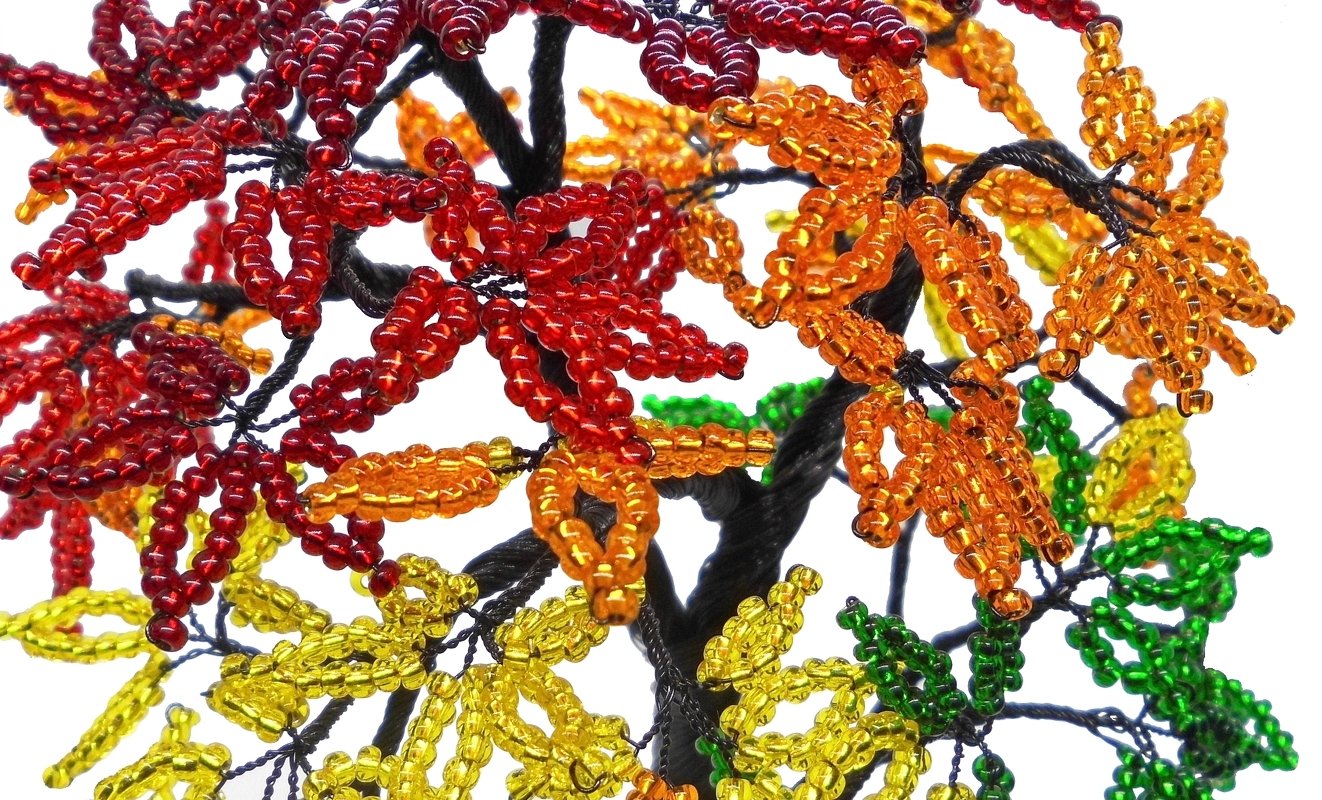 Close-up of a beaded wire tree with red, orange, yellow and green seed-bead leaves on a twisted dark wire trunk