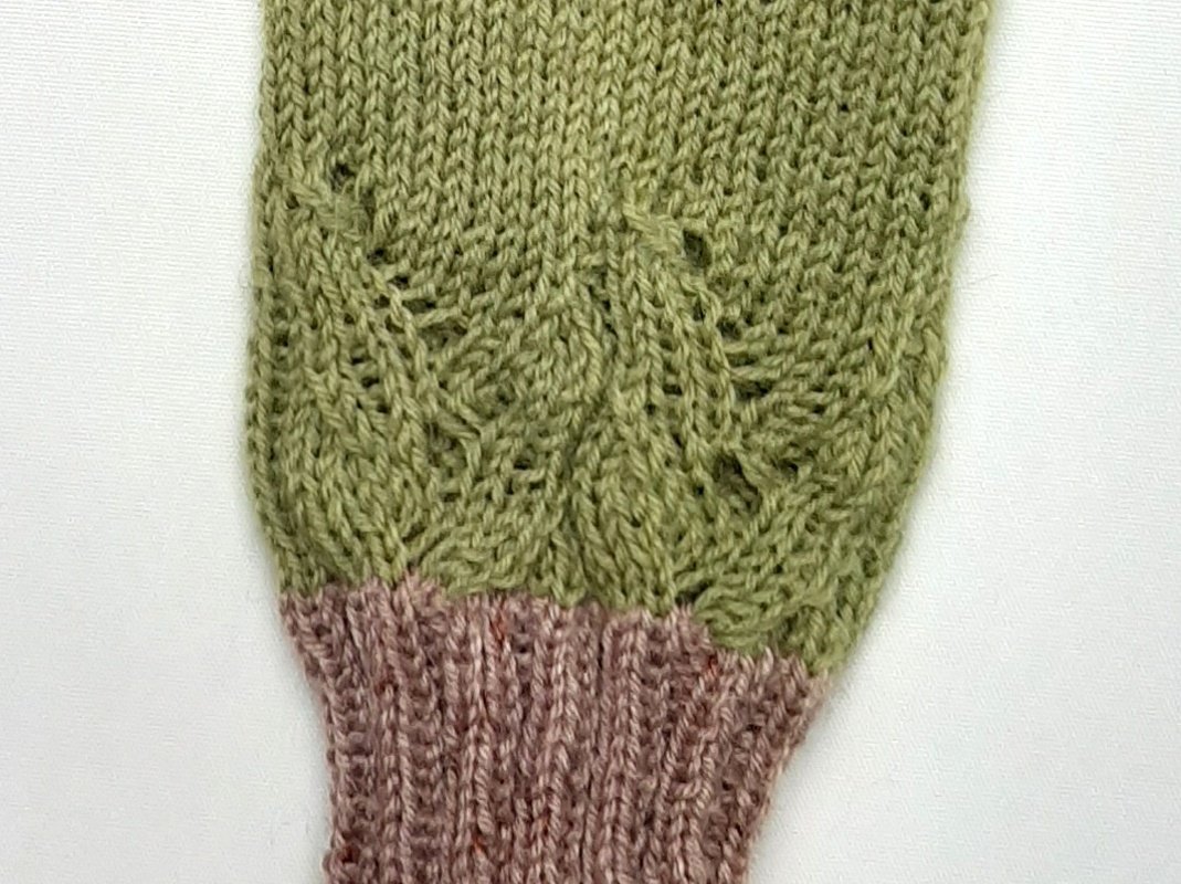 Gestrickte grün-rosa Armstulpe mit Blattmuster und rosa Rippbündchen