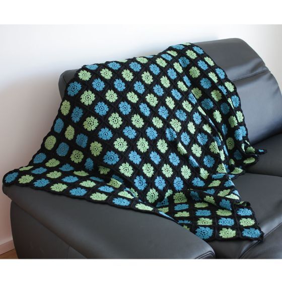 Gehäkelte Decke aus blauen und grünen Granny-Squares mit schwarzer Umrandung auf grauem Sofa