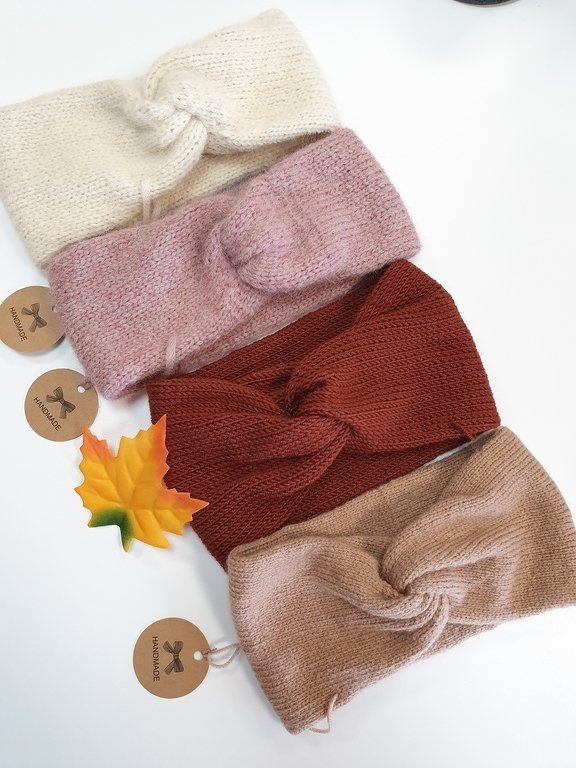 Vier gestrickte Stirnbänder in Creme, Altrosa, Rostrot und Beige mit Twist-Knoten und runden Anhängern auf weißem Hintergrund.
