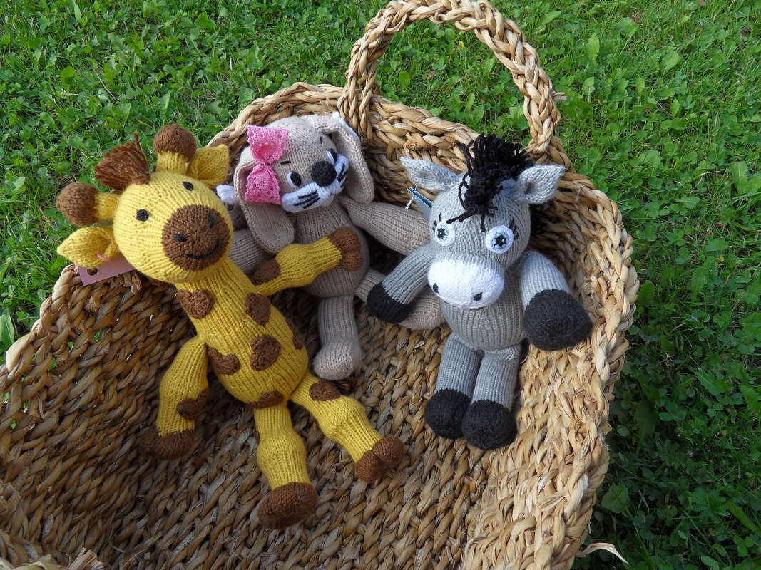 Gestrickte Amigurumi Giraffe, Hase und Esel in einem Korb auf Gras