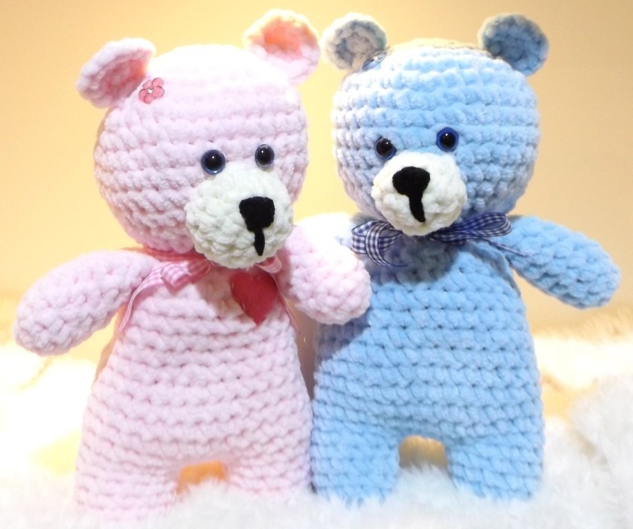 Zwei gehäkelte Amigurumi-Teddys, einer rosa mit Herzanhänger, einer blau mit karierter Schleife