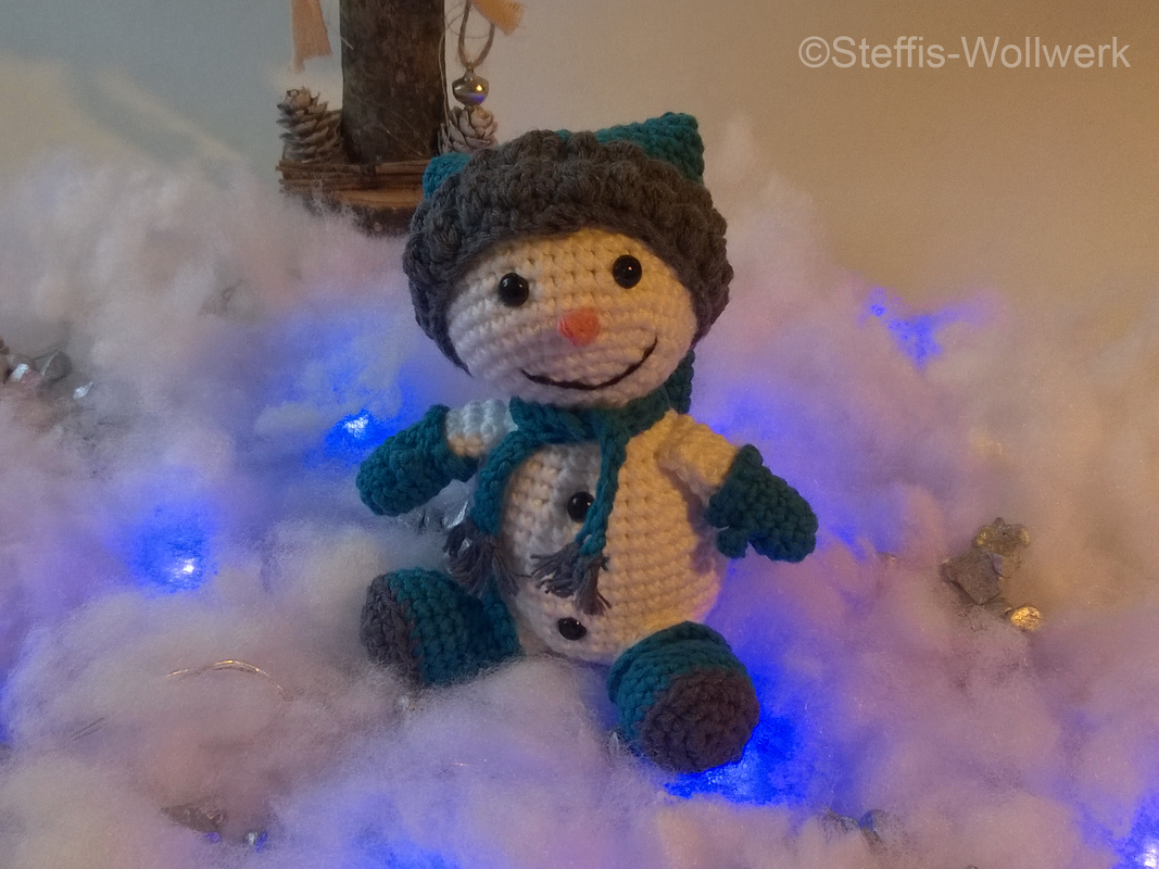 Gehäkelter Schneemann mit Mütze, Schal und Handschuhen, sitzend auf Kunstschnee mit blauen Lichtern
