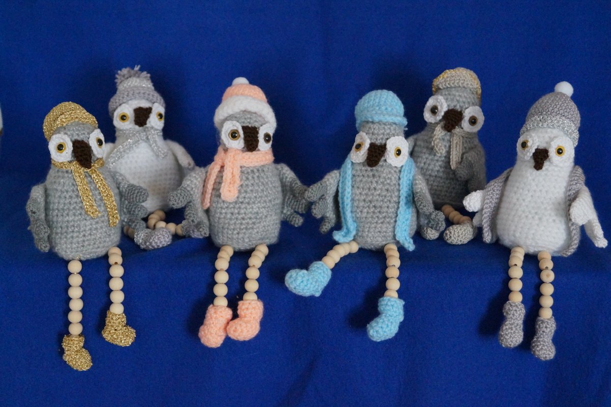 Mehrere winterliche Amigurumi-Eulen in Grau mit bunten Mützen und Schals auf blauem Hintergrund