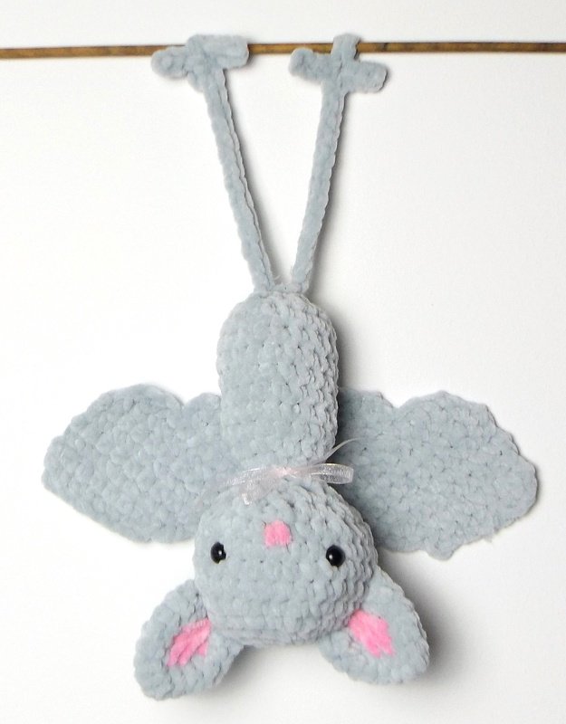 Niedliche, hellgraue Amigurumi‑Fledermaus mit rosa Details, kopfüber hängend