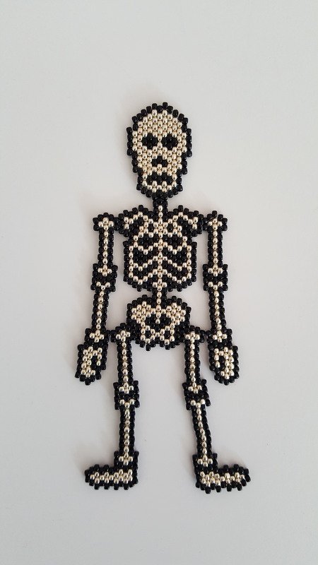 Gefädeltes Skelett aus schwarzen und silbernen Perlen auf hellem Hintergrund.