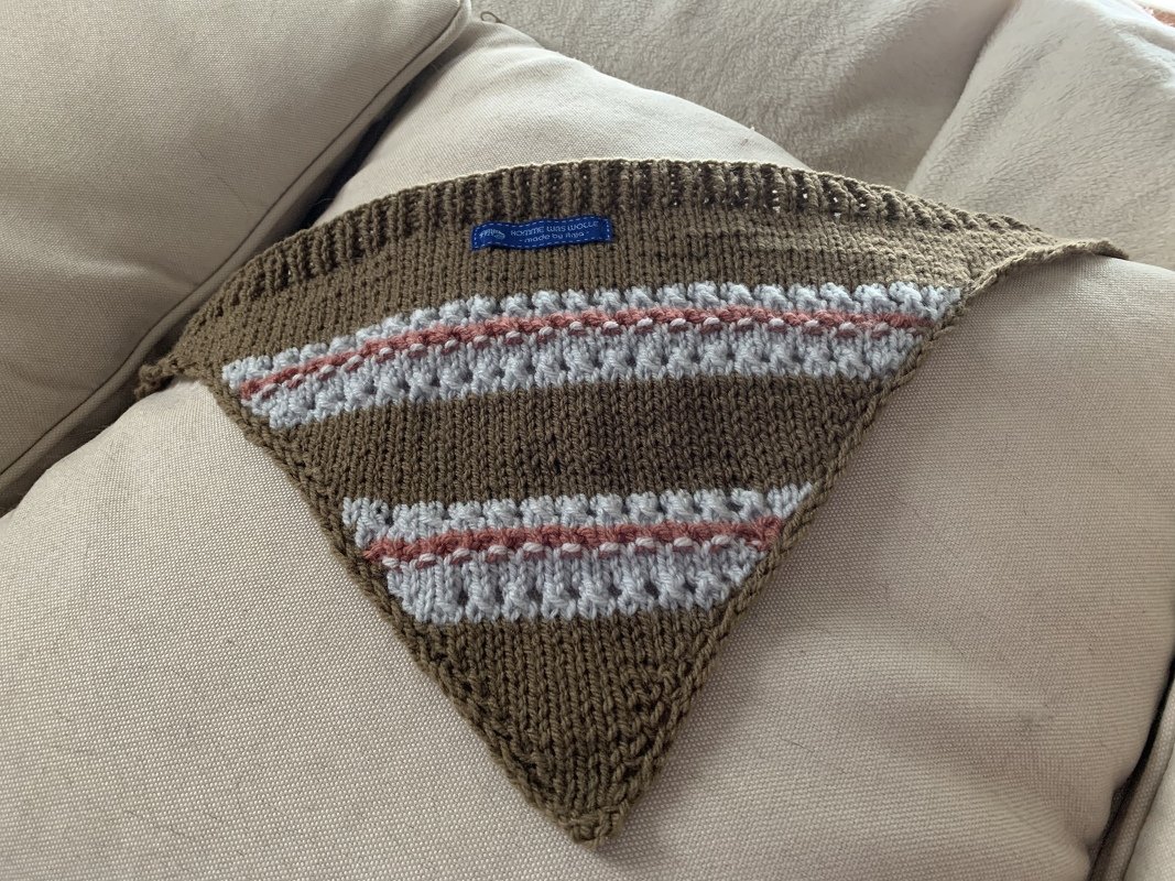 Gestricktes dreieckiges Halstuch für Haustiere in Braun mit hellblauen und rosa Streifen auf hellem Kissen.