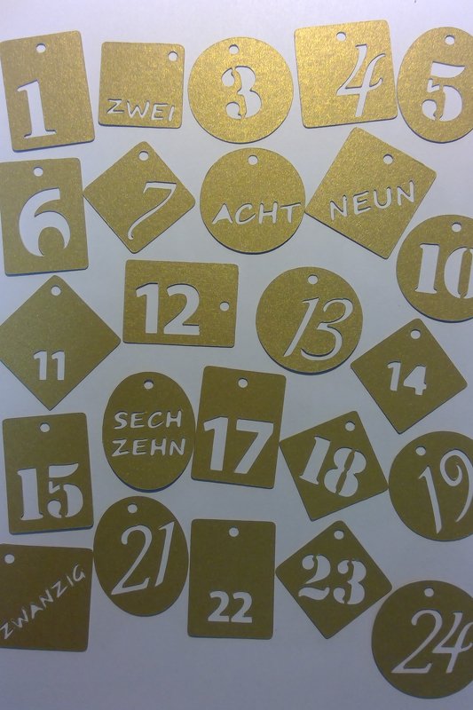 Goldene Adventsanhänger mit Zahlen und ausgeschriebenen Zahlwörtern 1–24 in verschiedenen Formen, teils mit Aufhängeloch