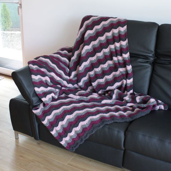 Gehäkelte Zickzack-Decke in Rosa, Grau und Dunkelrot auf schwarzem Sofa
