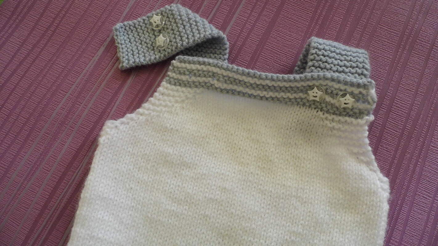weiß gestrickter Trägerstrampler mit grauen knöpfbaren Trägern und passendem Stirnband