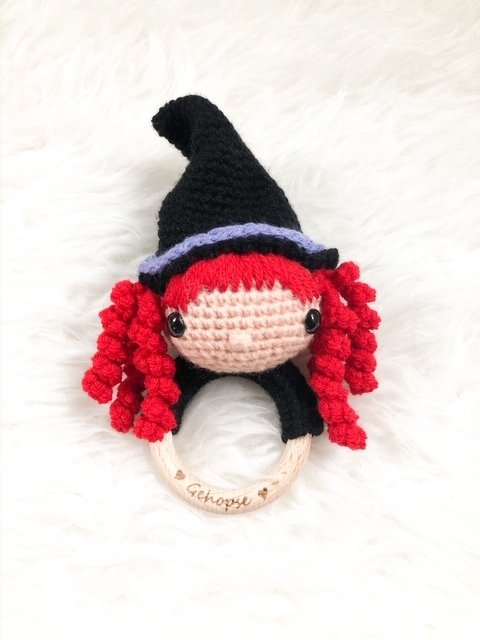 Gehäkelte Hexen-Rassel mit roten Locken und schwarzem Hut an einem Holzring