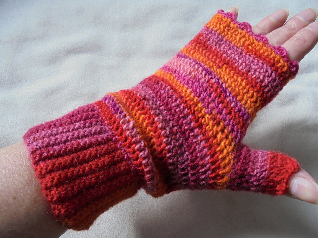 Nahaufnahme eines gehäkelten fingerlosen Handschuhs mit pink-, orange- und roten Streifen, an einer Hand getragen.