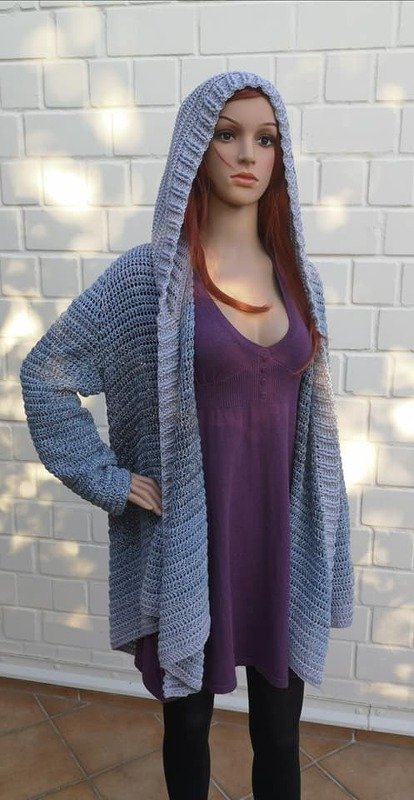 Schaufensterpuppe zeigt offen getragene gehäkelte Kapuzenjacke in Blau‑Grau-Ombré über violettem Kleid
