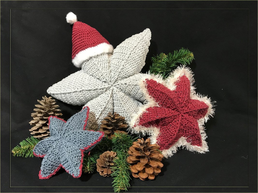 Drei gehäkelte Weihnachtssterne in Grau, Rot und Blaugrau mit Weihnachtsmütze, flauschigem Rand, Tannenzapfen und Nadelzweigen.
