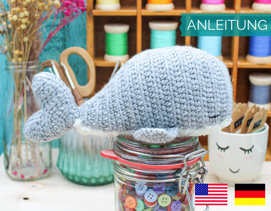 Gehäkelter grauer Amigurumi-Wal mit gesticktem Auge auf Glasdose mit Knöpfen