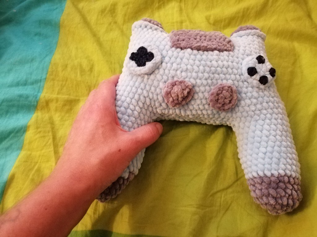 Hand hält gehäkelten Gamecontroller in Hellblau und Mauve