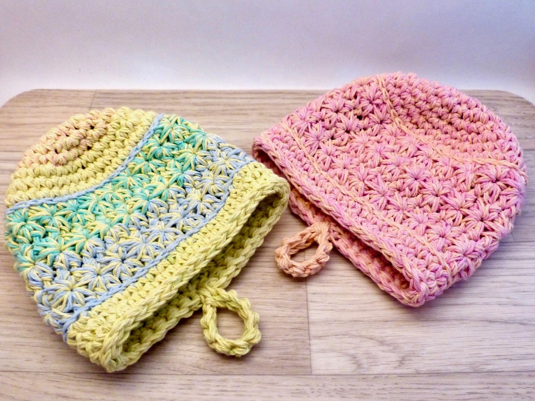 Nahaufnahme zweier gehäkelter Topflappen mit sternähnlichem Muster und Aufhängeschlaufen